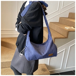 Détail du grand sac hobo en jean bleu avec cordon de serrage et logo en cuir marron