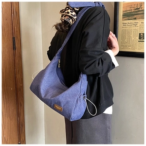 Détail du sac croissant en denim bleu avec cordon de serrage et écusson en cuir brun