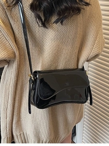 Glossy black patent leather shoulder bag with gold hardware and curved flap design