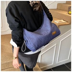 Détail du sac cabas en denim bleu avec cordons latéraux et patch de marque en cuir
