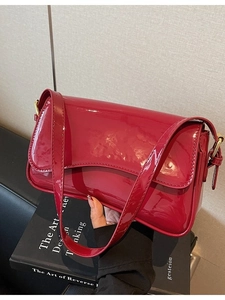 Red glossy patent leather shoulder bag with gold hardware in a stylish lifestyle setting