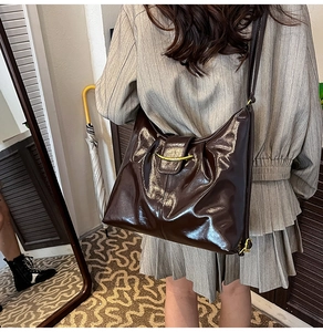 Detailed shot of dark brown glossy hobo bag with gold metal hardware on model