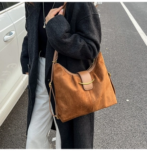 Detail of a brown suede hobo bag featuring a crescent gold buckle and leather strap