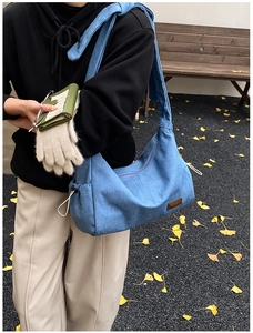 Détail d'un sac bandoulière en denim bleu avec logo en cuir et fermeture à cordon