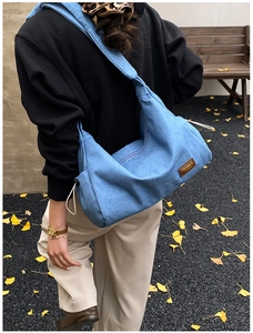Détail du sac hobo en jean bleu avec cordon de serrage et logo en cuir sur feuilles