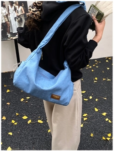 Vue de rue extérieure d'un grand sac bandoulière en denim bleu avec étiquette en cuir