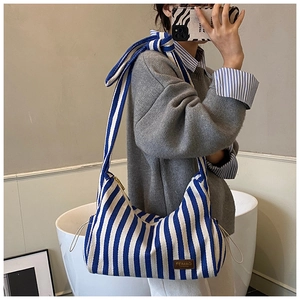 Détail du sac hobo en toile rayée bleue et blanche avec écusson en cuir marron