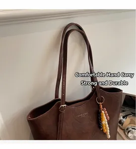 Dettaglio della borsa tote in pelle marrone scuro con scritte dorate e ciondolo di perline