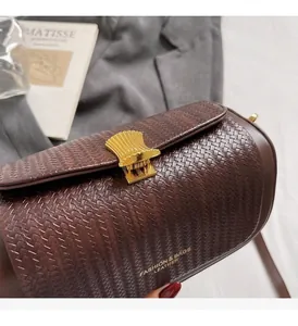 Close-up detail of a brown woven leather box bag featuring an elegant golden shell clasp