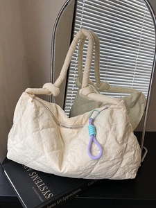 Quilted cream puffer shoulder bag with knot handle and woven charm shown in modern setting