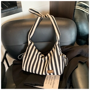 Détail du sac hobo en toile rayée avec étiquette en cuir sur un fauteuil en cuir noir