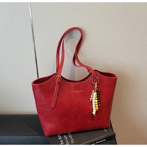 Dettaglio della borsa tote vintage in pelle rossa con trama granulosa e ciondolo di perline