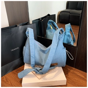 Détail d'un sac hobo en denim bleu clair avec bandoulière nouée et étiquette en cuir brun