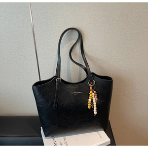 Dettaglio della borsa tote in pelle nera martellata con ciondolo di perline e metallo