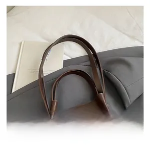 Detail of deep brown leather tote bag handle featuring reinforced metal rivets and stitching