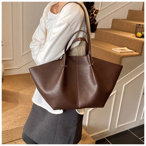 Detail view of a large brown tote bag with wing expansion worn by a model in a cozy setting