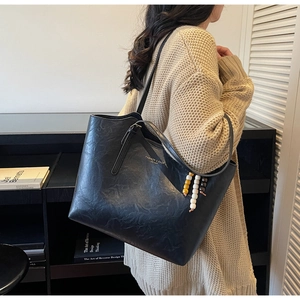 Dettaglio borsa tote in pelle nera con ciondolo di perle e logo con scritte dorate