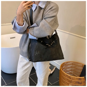 Detail of a large black leather tote bag with gold buckle on a shoulder-carried model