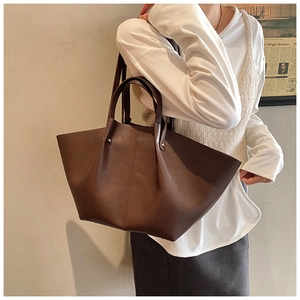 Detail view of large dark brown retro tote bag shown on a model against a clean wall