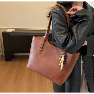 Dettaglio borsa tote marrone vintage con ciondolo di perline e logo dorato inciso