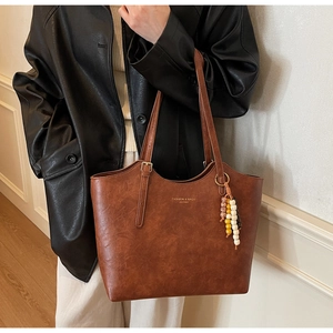 Dettaglio della borsa tote marrone in ecopelle con ciondolo di perline e logo dorato