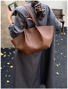 Detail of dark brown leather tote bag with wing design shown on a model in autumn scenery