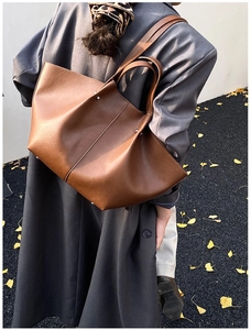 Outdoor street view of a large brown leather tote bag with silver studs on a model