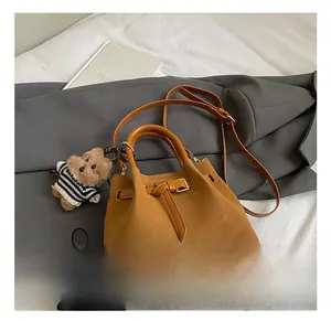 Détail d'un sac cabas en cuir marron avec breloque d'ours sur un drap blanc doux