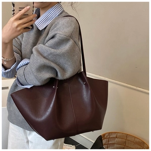 Detail view of large burgundy faux leather tote bag with metallic rivet accents on a model