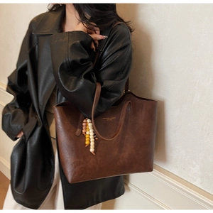 Dettaglio borsa tote marrone scuro con trama in pelle e ciondolo di perline colorate