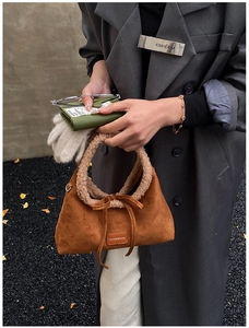 Dettaglio di una borsa in camoscio marrone con manico in shearling e fiocco decorativo