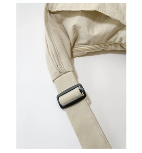 Detail of adjustable strap and black buckle on a beige nylon commuter hobo shoulder bag