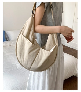 Detail of beige large nylon crescent bag showing side pocket and wide shoulder strap