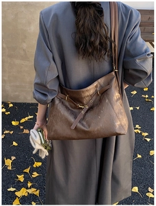 Detail view of a large brown hobo tote bag with strap on a model in autumn leaves