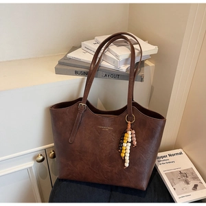 Dettaglio borsa tote vintage in pelle marrone con ciondolo di perline colorate e logo oro