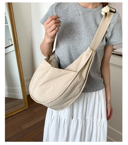 Close-up of beige nylon crescent bag with wide shoulder strap worn by a model