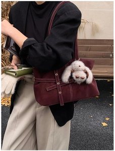 Detail of burgundy tote bag with rivet straps and plush bunny charm in autumn setting