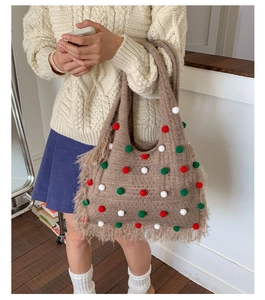 Detail of light brown knitted tote bag with festive pompoms and tassels on a cozy outfit