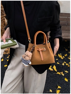 Détail du sac cabas en daim avec boucle décorative et breloque ourson dans un décor d'automne