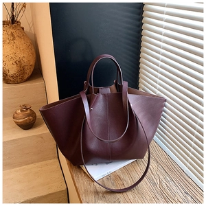Detail of burgundy bat-wing tote bag with premium leather texture and dual straps