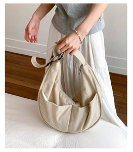 Detail of adjustable strap and large side pocket on beige nylon crescent shoulder bag