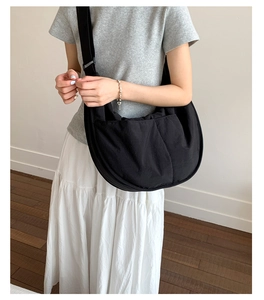 Detail of a large black nylon crescent crossbody bag worn by a model in casual style