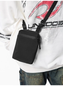 Detail of a black crossbody phone bag with waterproof zipper on an oversized hoodie