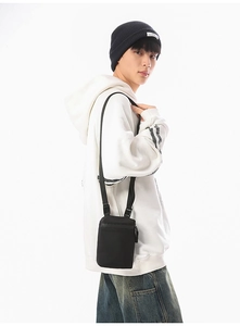 Man wearing a minimalist black nylon crossbody bag over a white hoodie in a street style look