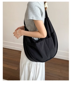 Detail shot of a large black nylon crescent messenger bag with dual front pockets on a model