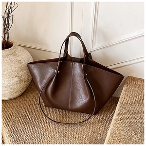 Detail of dark brown leather tote bag with wing-shaped pleats on textured surface