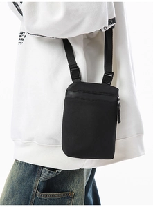 Detail of compact black nylon crossbody phone bag with adjustable straps on a white hoodie