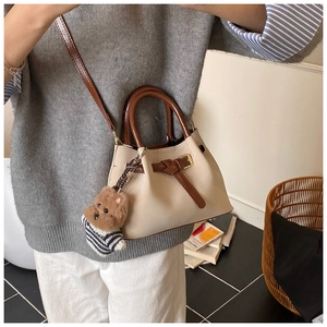 Détail d'un sac bandoulière crème avec poignée marron et charmant pendentif ours