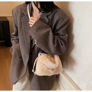 Détail du sac seau en peluche crème porté par un mannequin en costume gris