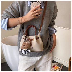 Détail du sac seau beige avec lanières brunes et un charmant petit ours en peluche